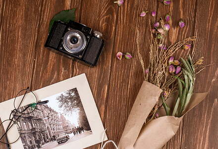 top-view-photo-glasses-old-camera-with-white-color-dry-branches-craft-paper-dry-rose-buds-scattered-wood