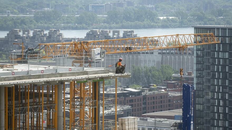 Un ouvrier de la construction travaille sur un immeuble en hauteur et on aperçoit une grue à l'arrière.