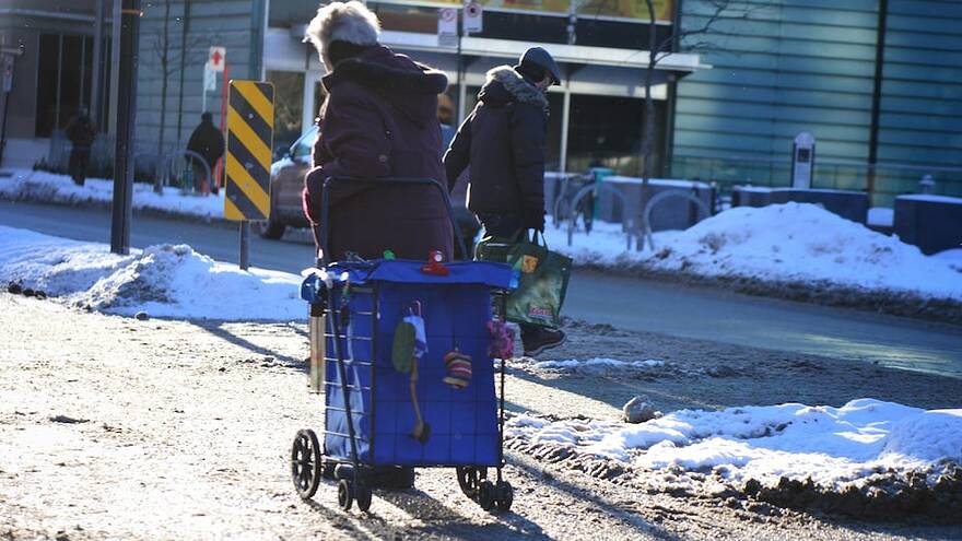 Un itinérant traîne son chariot dans la neige.