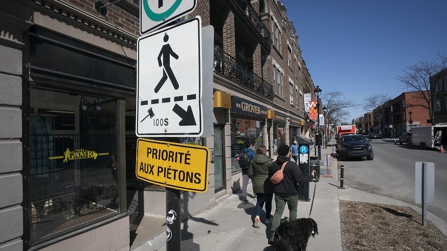 Des Montréalais marchent sur le trottoir, près d'une pancarte indiquant un passage réservé aux piétons.