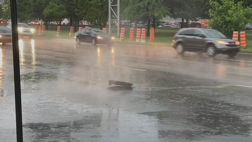 Un couvercle d'égout soulevé sur une rue où tombe une forte pluie.