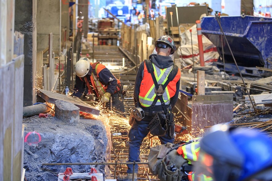 Des ouvriers sont en train de préparer l’armature de la semelle de béton sur laquelle sera érigé le quai de la station. Un tunnel piétonnier souterrain la reliera directement à la ligne verte du métro.