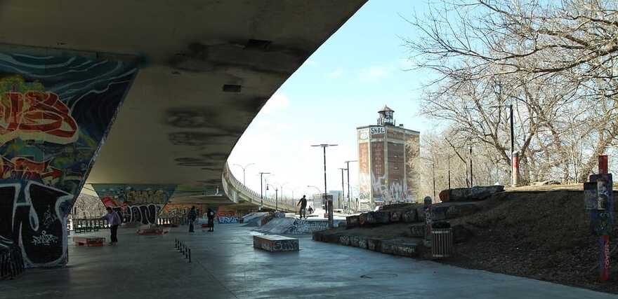 Une photo prise sous le viaduc, avec des gens qui font de la planche à roulette et, en arrière-plan, l'entrepôt Van Horne.