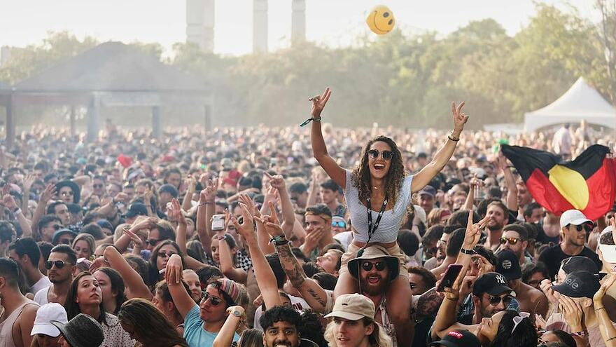 Photo d'une foule en plein concert extérieur avec des gens qui lèvent les bras dans les airs.