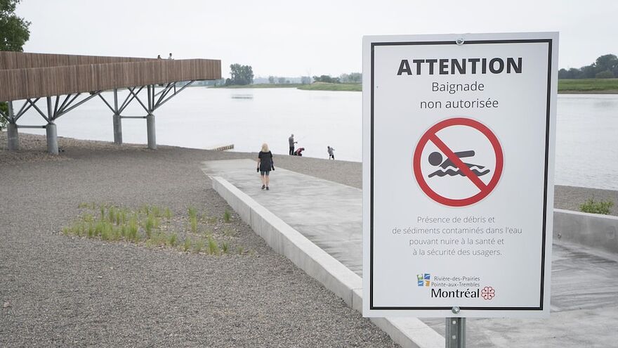 Quelques personnes sur le bord du fleuve, près d'une affiche d'interdiction de baignade.