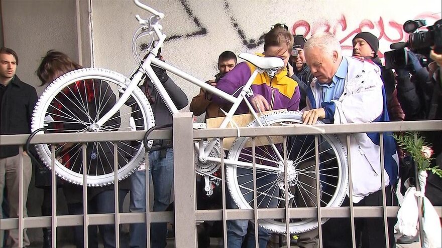 Des gens sont réunis autour du vélo peint en blanc en hommage à la cycliste Mathilde Blais