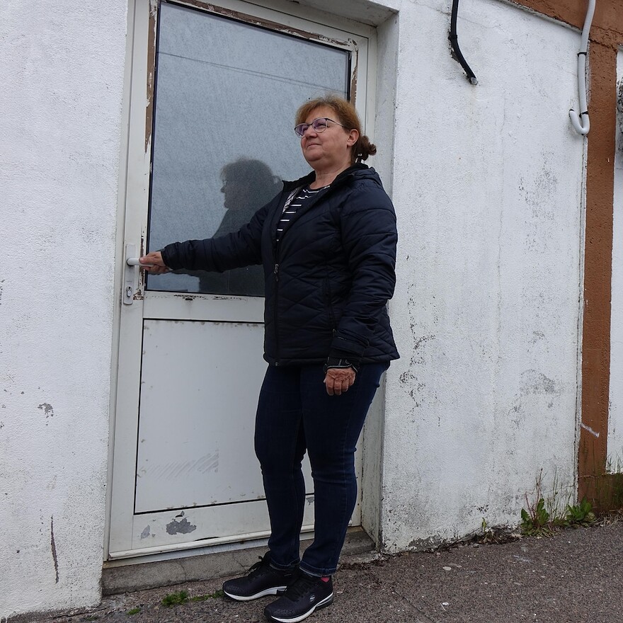 Une femme est devant un bâtiment et tiens la poignée de la porte.