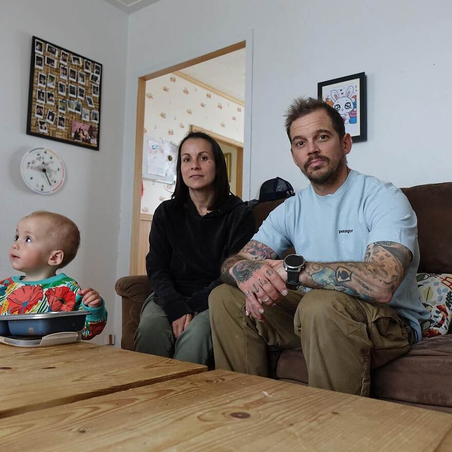 Un couple dans la trentaine sont assis dans leur salon avec leur jeune enfant debout devant eux.