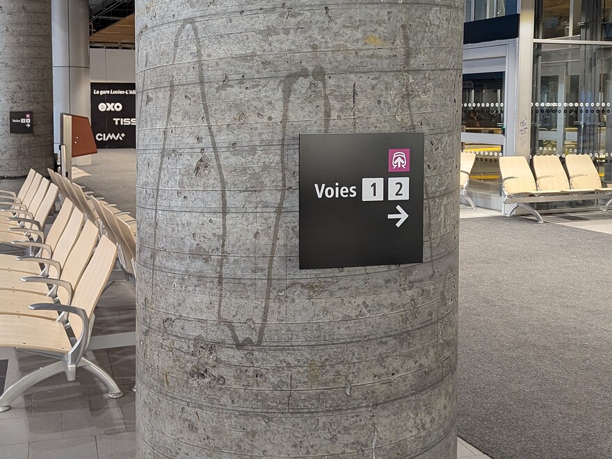 Petit panneau sur une colonne en béton brut indiquant l'emplacement des voies 1 et 2