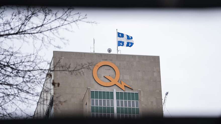 Zoom sur le logo installé en haut du bâtiment d'Hydro-Québec, avec un drapeau du Québec qui flotte sur le toit.