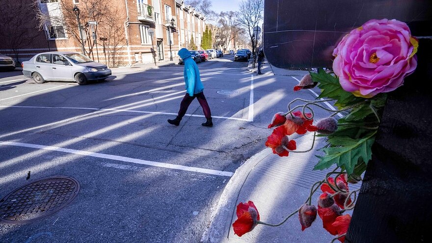 Un piéton traverse la rue. En bordure de la rue, des passants ont déposé des fleurs.