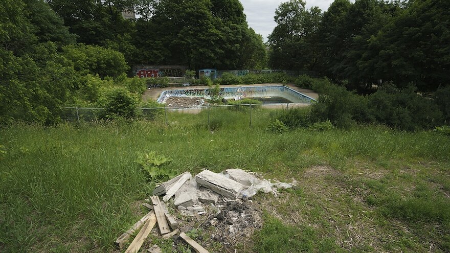 L'ancienne piscine publique à l'abandon, couverte de graffitis, tandis qu'on voit des débris à l'avant.