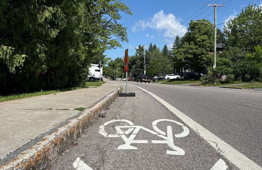 Une pancarte de signalisation temporaire placée directement dans la voie cyclable de la route de l'Aéroport.