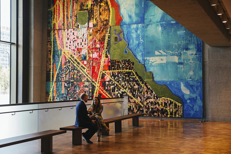 Visitors sit in front of Mark Bradford's "City of the Big Shoulders", a colorful multimedia piece that extends from the mezzanine to the first floor. Lucy Hewett for NPR