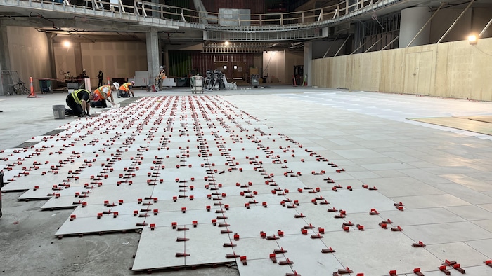 Des travailleurs de la construction posent du carrelage sur une grande surface.