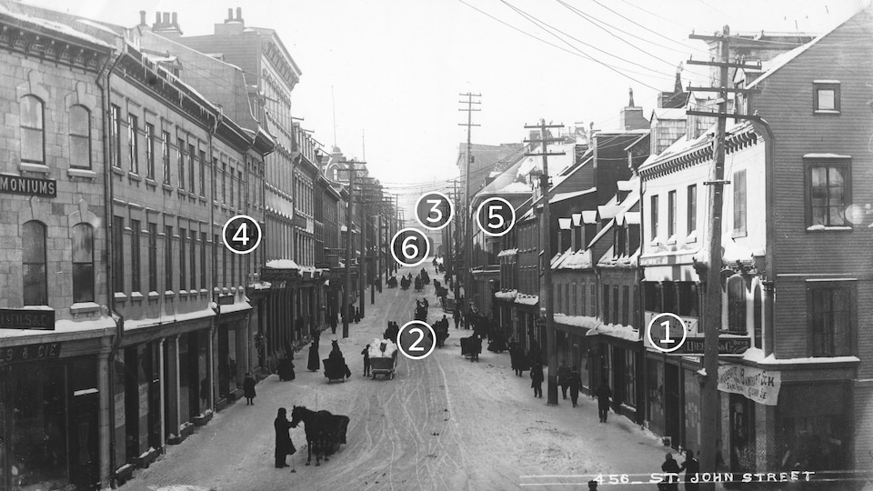 Image d'époque en noir et blanc, prise en hauteur, montrant la rue St-Jean en hiver, pleine de passants.