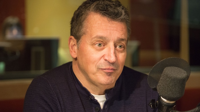 Il regarde devant lui, assis derrière un micro.