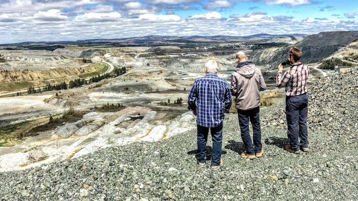 Trois hommes de dos regardent un paysage minier, très gris à perte de vue.