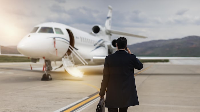Un homme d'affaires qui parle au téléphone marche vers un jet privé sur un tarmac.