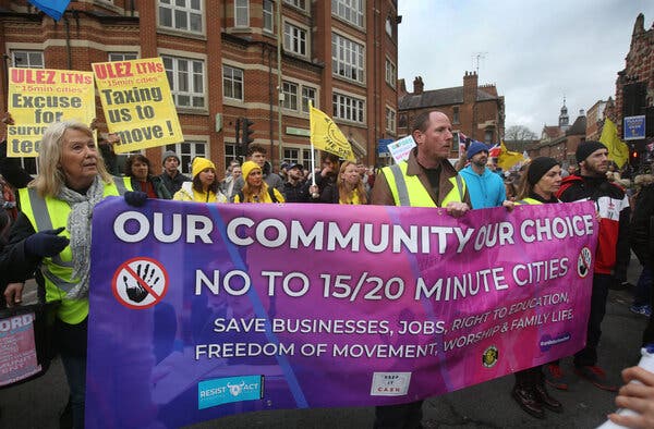 A crowd of people carry a banner that reads, “Our Community, Our Choice. No to 15/20 minute cities. Save businesses, jobs, right to education, freedom of movement, worship & family life.”