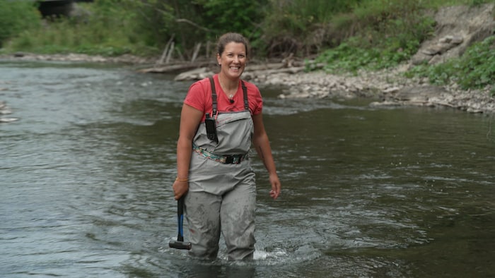 Une femme en combinaison marche dans une rivière.