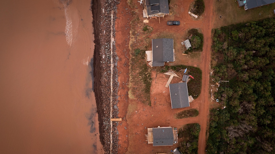 Photo aérienne prise directement au-dessus d'une région côtière. On voit la terre rouge, de l'eau brune et les débris de bâtiments endommagés par l'ouragan.
