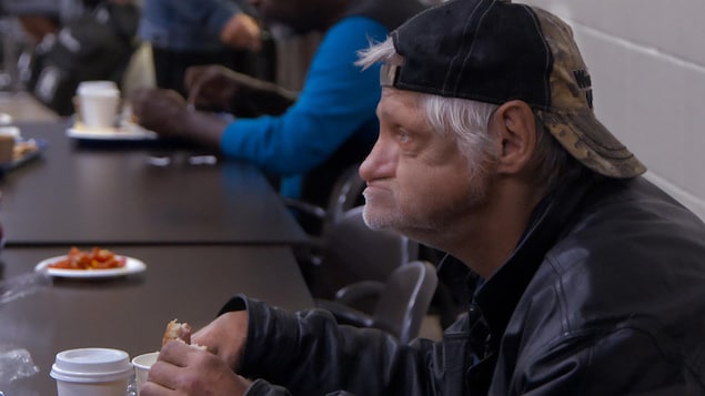 Un homme mange à la table d'une salle communautaire.