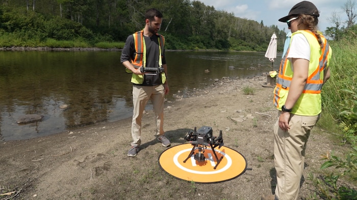 Un homme et une femme regardent un drone transportant une caméra thermique, sur le bord d'une rivière.