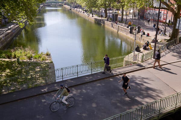 Pedestrians and cyclists cross a bridge over a river in Paris. The bridge and surrounding area are free of vehicles.