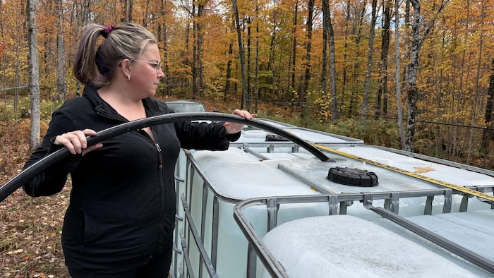 Une femme remplit un bidon d'eau avec un tuyau.