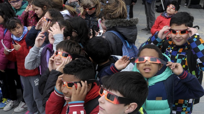 Des enfants observent une éclipse portant des lunettes.
