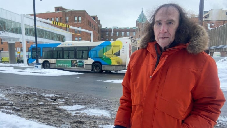 A man with a cane stands in front of a bus.
