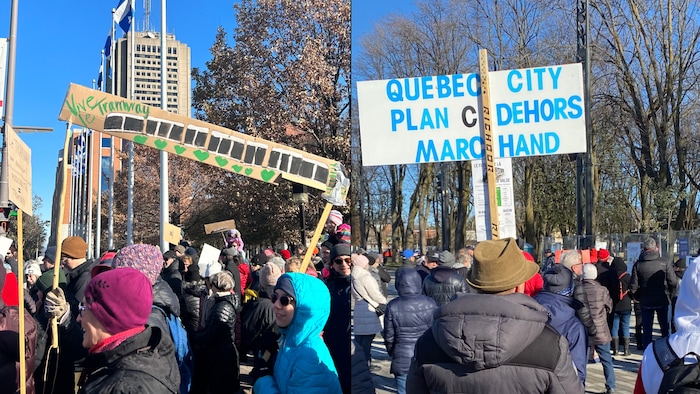 Deux manifestants tiennent des affiches, l'une sur laquelle un tramway est dessiné et l'autre où les mots "Quebec city, plan C dehors Marchand" sont inscrits.
