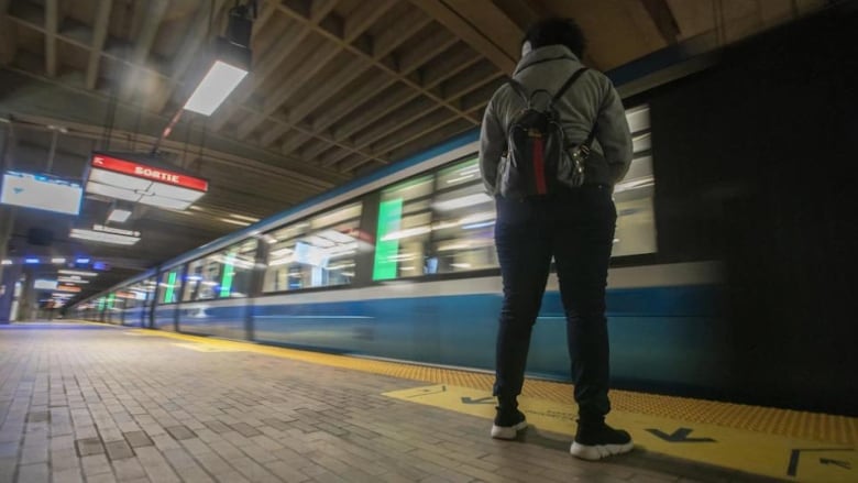 A commuter stands on the platform as a Montreal Metro whips by.