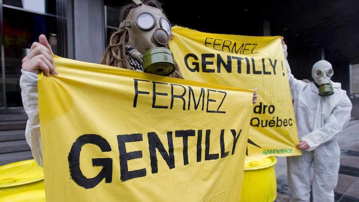 Des militants masqués tiennent une banderole indiquant : « Fermez Gentilly ».