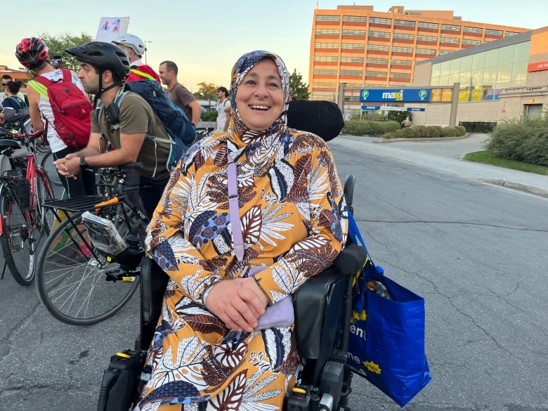 A woman wearing a colourful headscarf and matching patterned dress smiles in a wheelchair.