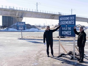 Federal Conservative Party Leader Pierre Poilievre and his Quebec lieutenant Pierre Paul-Hus point to a sign reading Build the Homes in an empty parking lot near a train track.