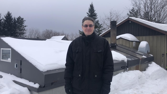 Daniel Perron se tient devant les bâtiments qui renferment le système de biomasse.