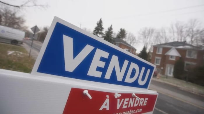 Pancarte « À vendre – Vendu » dans une rue résidentielle.