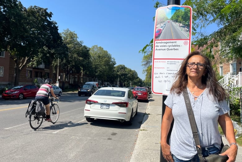 A woman stands next to a sign announcing roadwork to revamp bike lanes while a cyclist passes by.