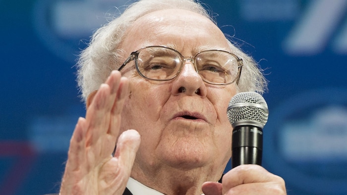 L'homme d'affaires Warren Buffett s'adressant à un public en tenant un micro dans sa main gauche.