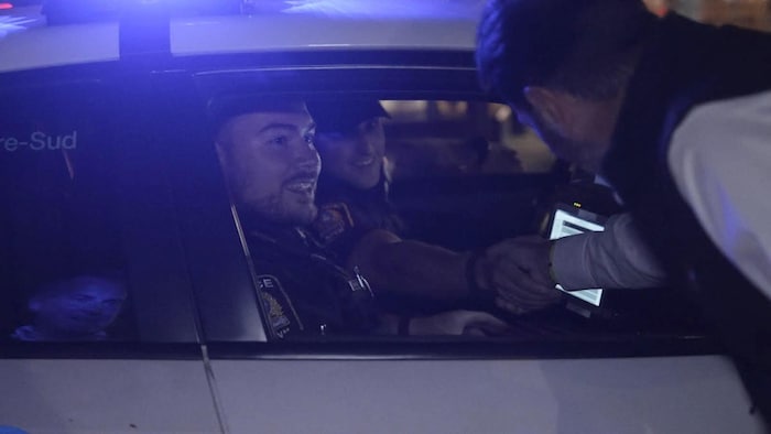 François Bonnardel, penché près de la fenêtre d'une voiture de patrouille, discute avec deux agents.