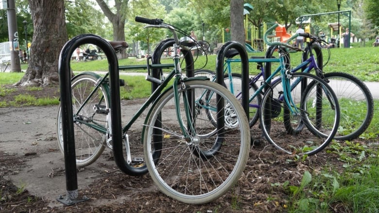 Three bicycles are locked to a bike rack in front of a park