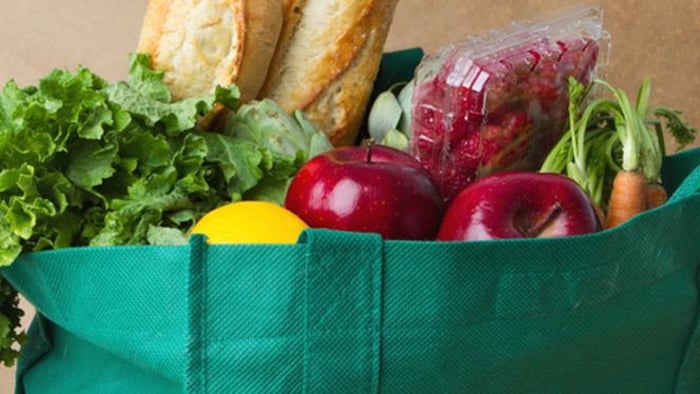 Un sac d'épicerie réutilisable vert est rempli de fruits et de légumes.