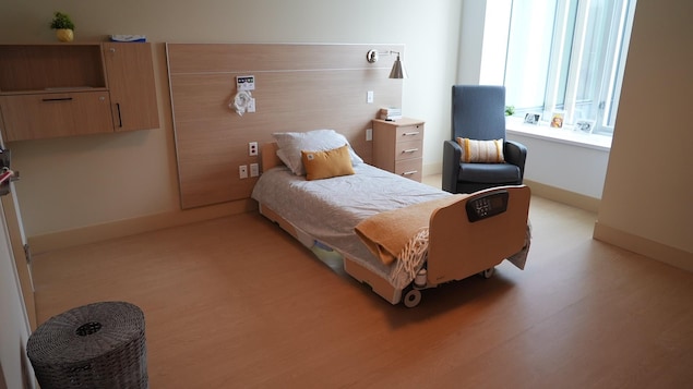 Une chambre avec un lit simple, une table de chevet et un fauteuil.
