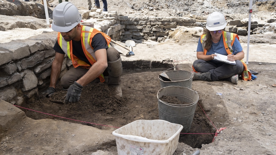 Deux archéologues accroupis fouillent dans un terrain.
