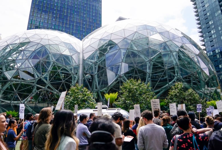 Dozens of people hold signs outside of a spherical glass building.
