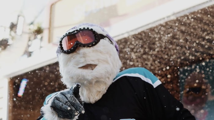 Une personne portant un masque de yéti avec des lunettes de ski danse sous les flocons.