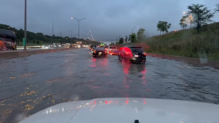 Des véhicules circulent lentement sur l'autoroute inondée.