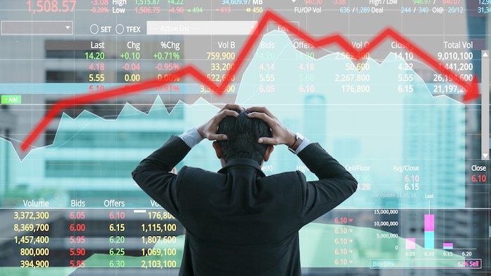 Image conceptuelle d'un homme d'affaires qui se saisit la tête devant des diagrammes et différents tableaux avec des chiffres et une flèche qui monte et descend.